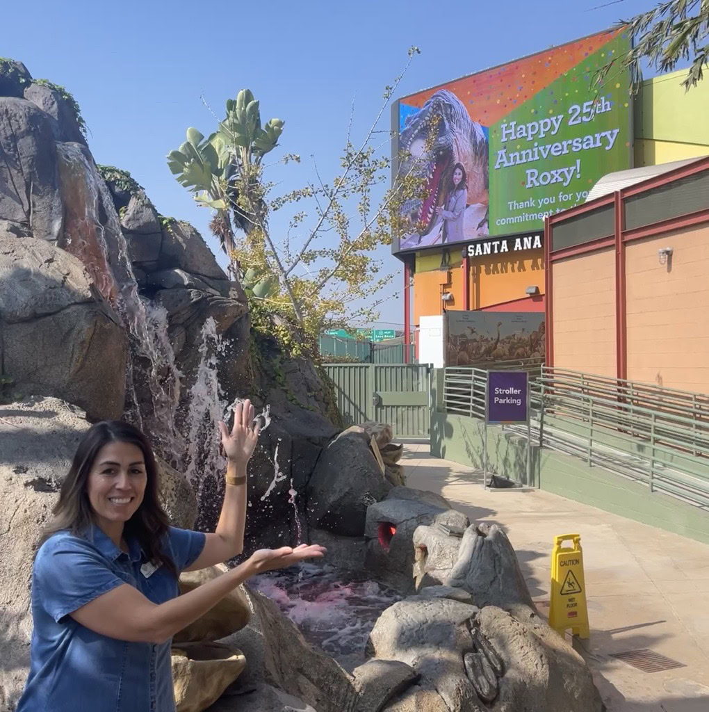 Roxy from Discovery Cube Orange County taking a photo in front of the billboard.
